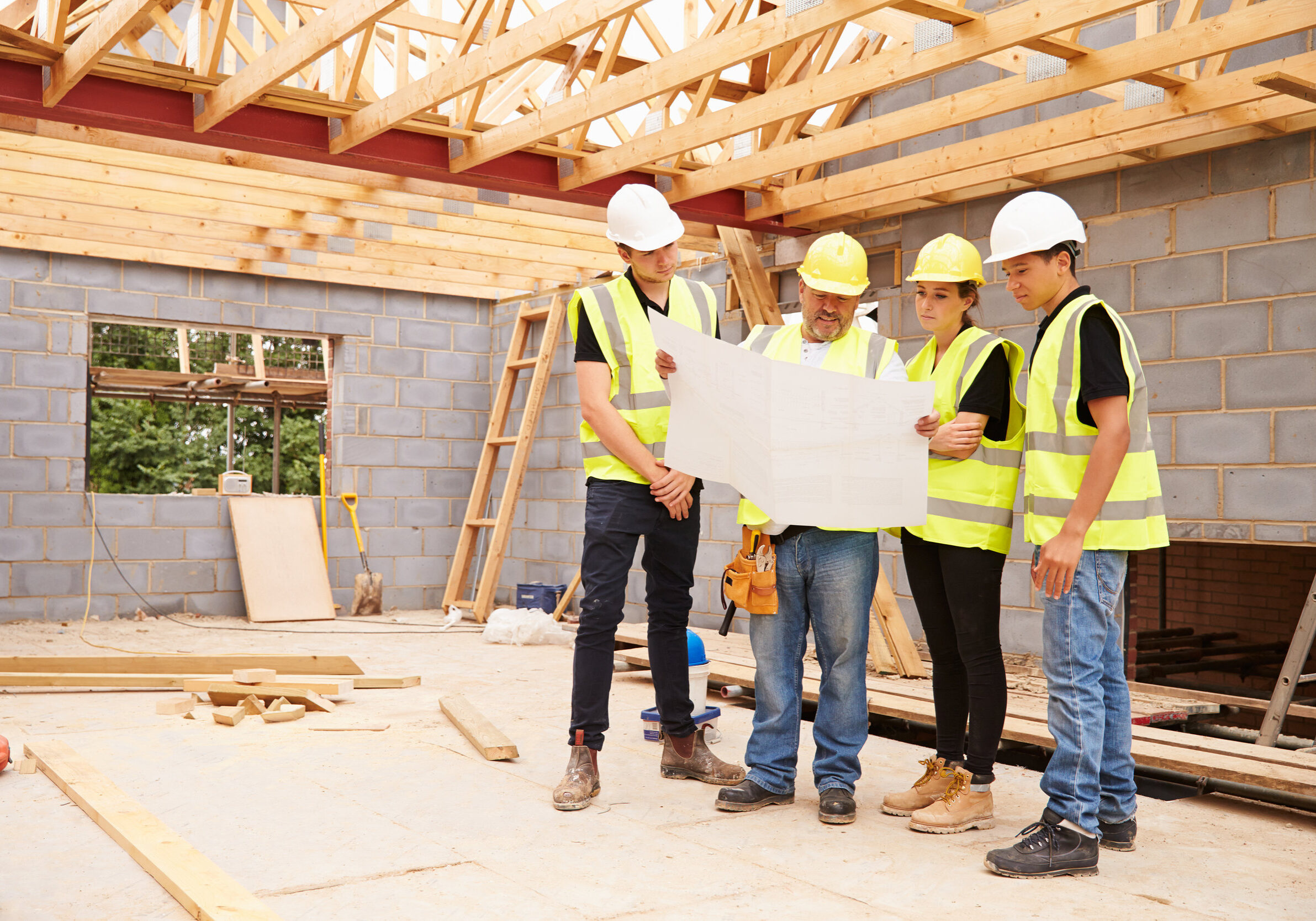 Builder On Building Site Looking At Plans With Apprentices